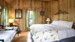 A wooden-paneled room with a bed, a chair, a table, and a window. - Peaceful Waterfront Cabin with Private Pond Near Zwolle, Louisiana (Zwolle)