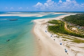 Uma praia costeira com águas cristalinas, faixa de areia e um pequeno povoado com casas e vegetação.