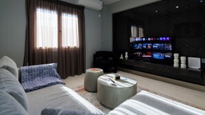 A modern hotel room with a large flat-screen TV, a sofa, two ottomans, and a large window with curtains. - 
Silk Luxury 1 bedroom Hideout in Vari (Vari)