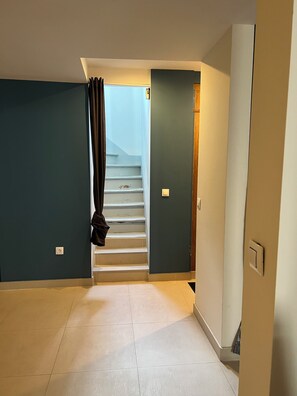 Ein Flur mit einer Treppe, die zu einer Zwischenebene führt, einem an der Wand hängenden Mantel und einem Lichtschalter.