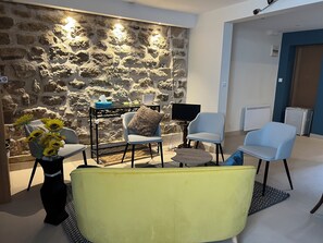 Ein modernes Wohnzimmer mit Steinwand, einem Flachbildfernseher und zwei hellblauen Sesseln.