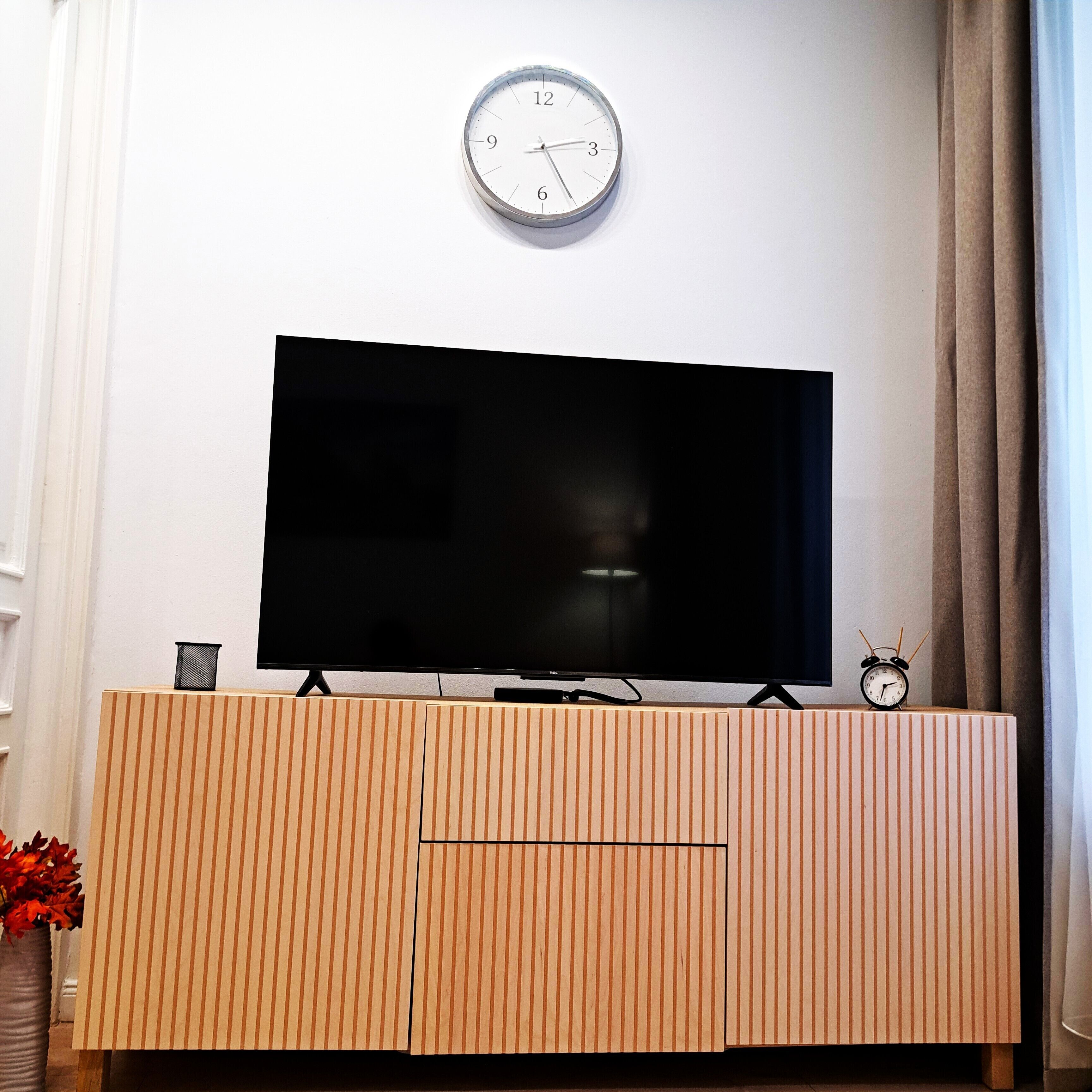 Una TV a schermo piatto su un mobile in legno, con una sveglia sopra.