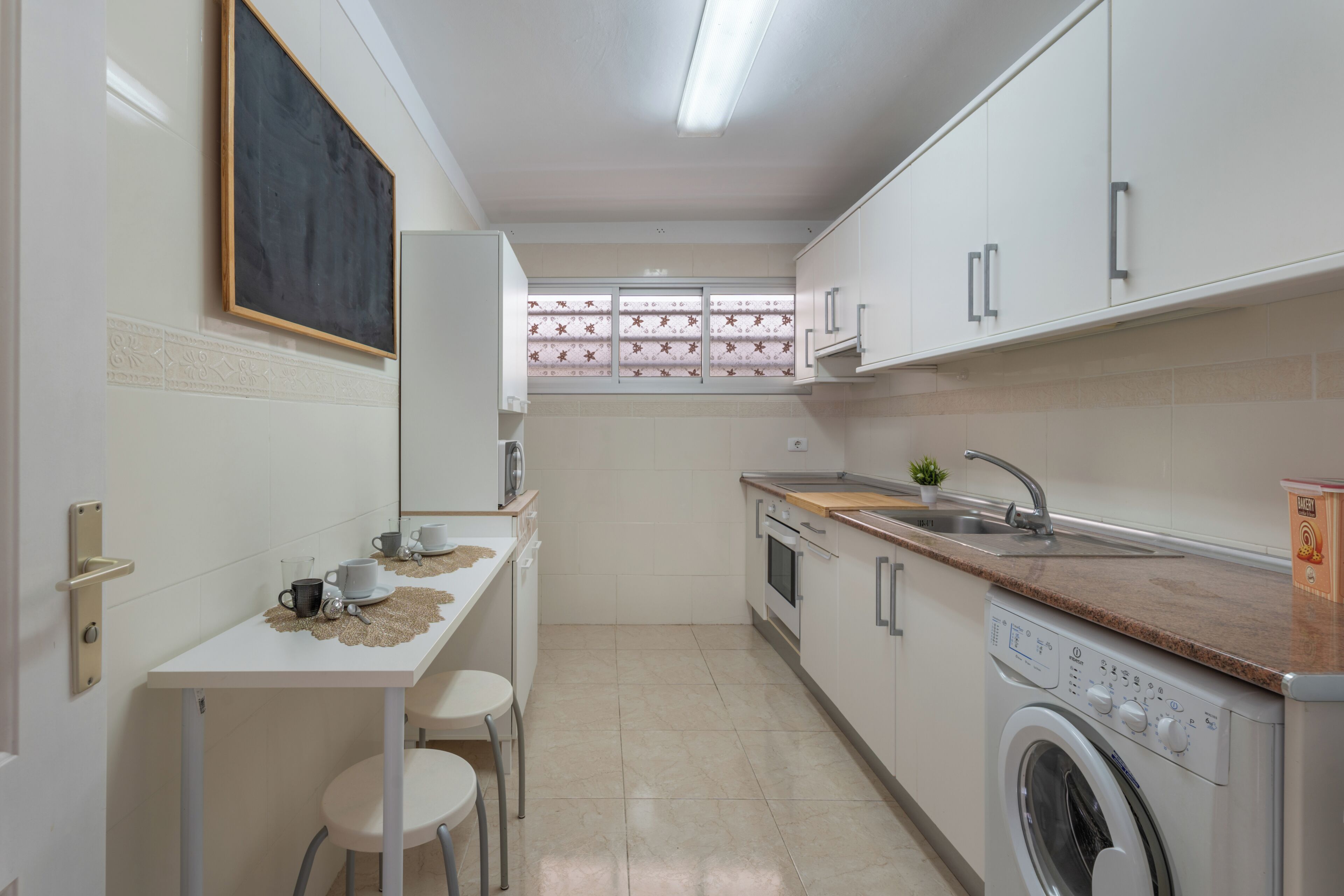 A compact kitchen with a washing machine, a sink, and a small table with chairs.