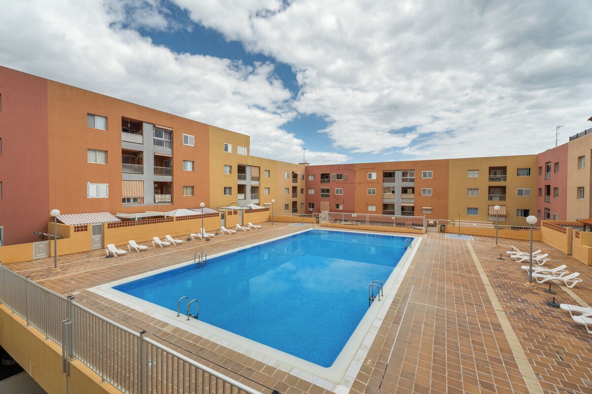 A swimming pool with lounge chairs, a tiled deck, and multi-story buildings with balconies.