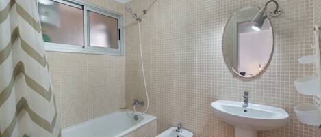 A bathroom with a bathtub, bidet, sink, and a mirror.