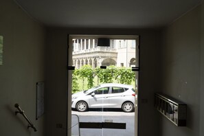 A doorway leading to a street with a white car parked outside. - GuestHost - Comfy ARIA Apartment near Cenisio (MM5) (Milan)