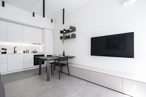 A modern kitchen with white cabinets, a dining table, and black shelves with plants. - GuestHost - Comfy ARIA Apartment near Cenisio (MM5) (Milan)