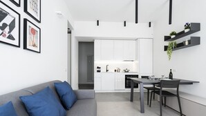 A modern kitchen with white cabinets, a dining table with chairs, and a grey sofa with blue cushions. - GuestHost - Comfy ARIA Apartment near Cenisio (MM5) (Milan)