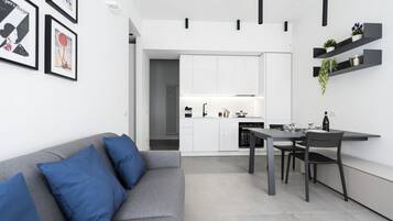 Eine moderne Küche mit weißen Schränken, einem Esstisch mit Stühlen und einem grauen Sofa mit blauen Kissen.