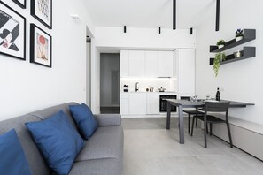 A modern kitchen with white cabinets, a dining table with chairs, and a grey sofa with blue cushions. - GuestHost - Comfy ARIA Apartment near Cenisio (MM5) (Milan)
