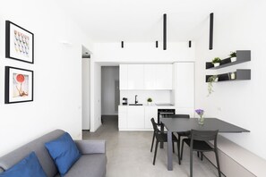 A modern kitchen with white cabinets, a dining table with chairs, and a gray sofa with blue cushions. - GuestHost - Comfy ARIA Apartment near Cenisio (MM5) (Milan)