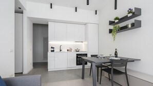 A modern kitchen with white cabinets, a dining table with chairs, and a built-in oven. - GuestHost - Comfy ARIA Apartment near Cenisio (MM5) (Milan)