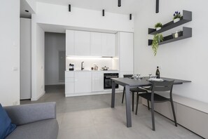 A modern kitchen with white cabinets, a dining table with chairs, and a built-in oven. - GuestHost - Comfy ARIA Apartment near Cenisio (MM5) (Milan)