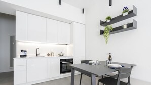 A modern kitchen with white cabinets, a built-in oven, and a dining area with a table and chairs. - GuestHost - Comfy ARIA Apartment near Cenisio (MM5) (Milan)