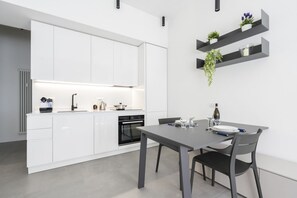 A modern kitchen with white cabinets, a built-in oven, and a dining area with a table and chairs. - GuestHost - Comfy ARIA Apartment near Cenisio (MM5) (Milan)