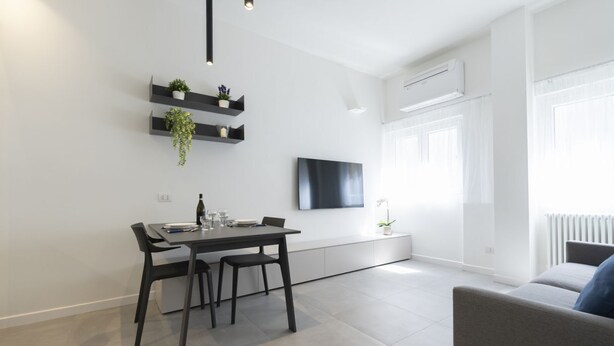A modern living space with a dining area, a flat-screen TV mounted on the wall, and a sofa. - GuestHost - Comfy ARIA Apartment near Cenisio (MM5) (Milan)