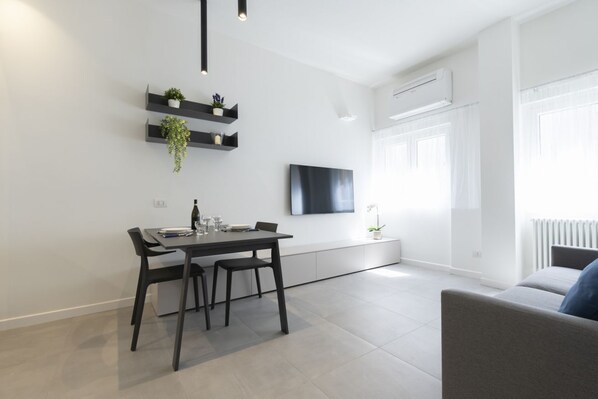 A modern living space with a dining area, a flat-screen TV mounted on the wall, and a sofa. - GuestHost - Comfy ARIA Apartment near Cenisio (MM5) (Milan)