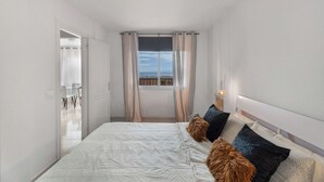 A bedroom with a bed, curtains, a window with a view, and a nightstand with a lamp. - Erma Sun & Pool - Apartment in Candelaria (Candelaria)