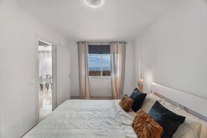 A bedroom with a bed, curtains, a window with a view, and a nightstand with a lamp. - Erma Sun & Pool - Apartment in Candelaria (Candelaria)