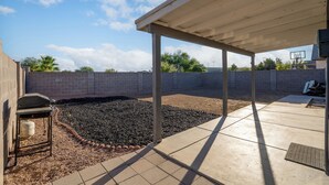 A covered patio area with a concrete floor, a grill, and a brick wall. - Group Home Near Stadium | Sleeps 14+ (El Mirage)