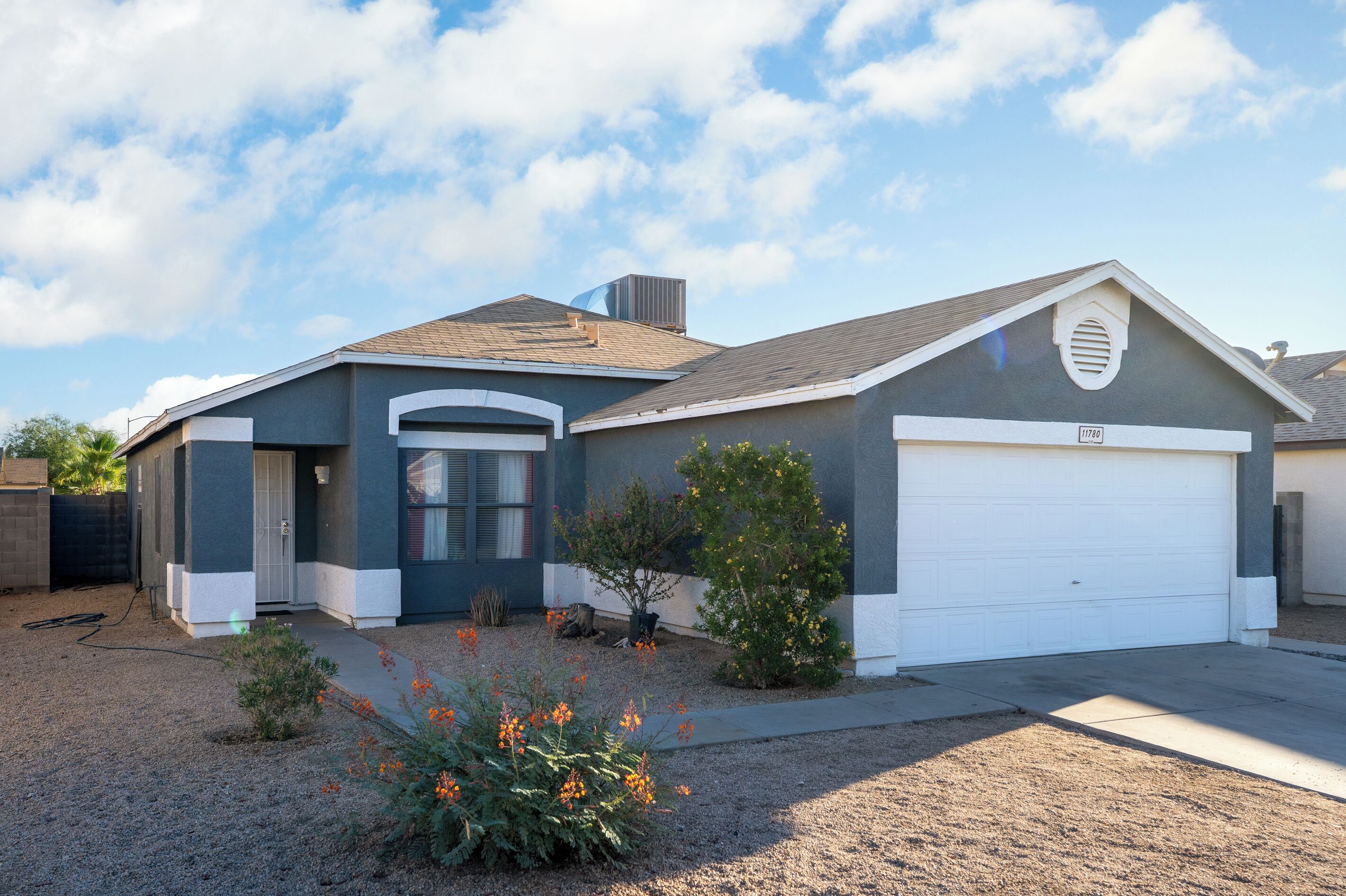 A single-story house with a garage, a small front yard with a gravel driveway, and a clear sky.