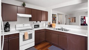 A modern kitchen with brown cabinets, white countertops, a stove, microwave, and a sink. - Group Home Near Stadium | Sleeps 14+ (El Mirage)