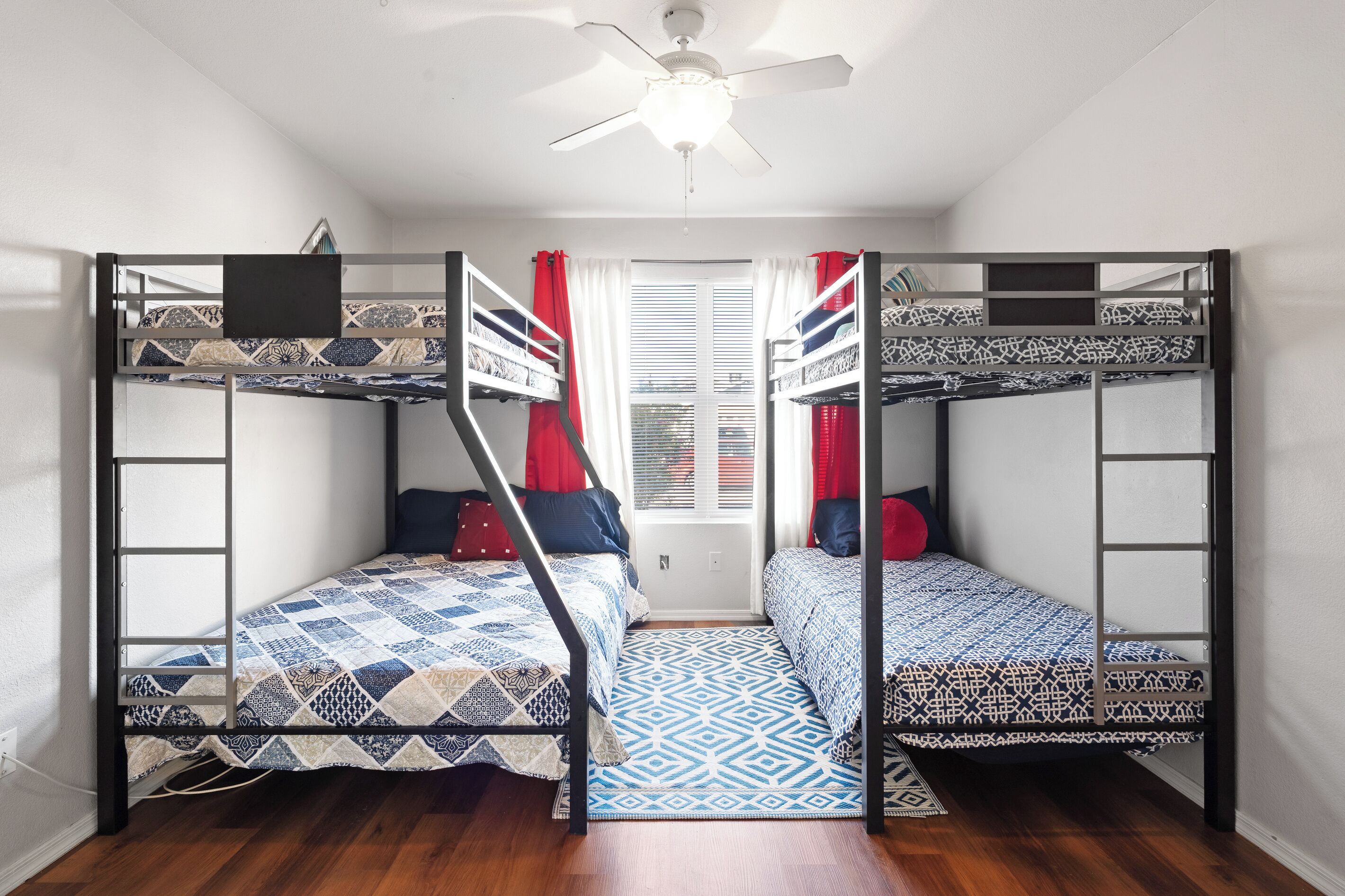A dormitory room with bunk beds, a ceiling fan, and a window with curtains.