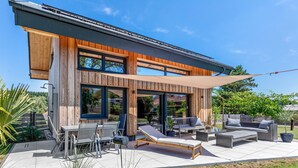 Una casa moderna con un patio, mobiliario exterior y un ventanal grande.