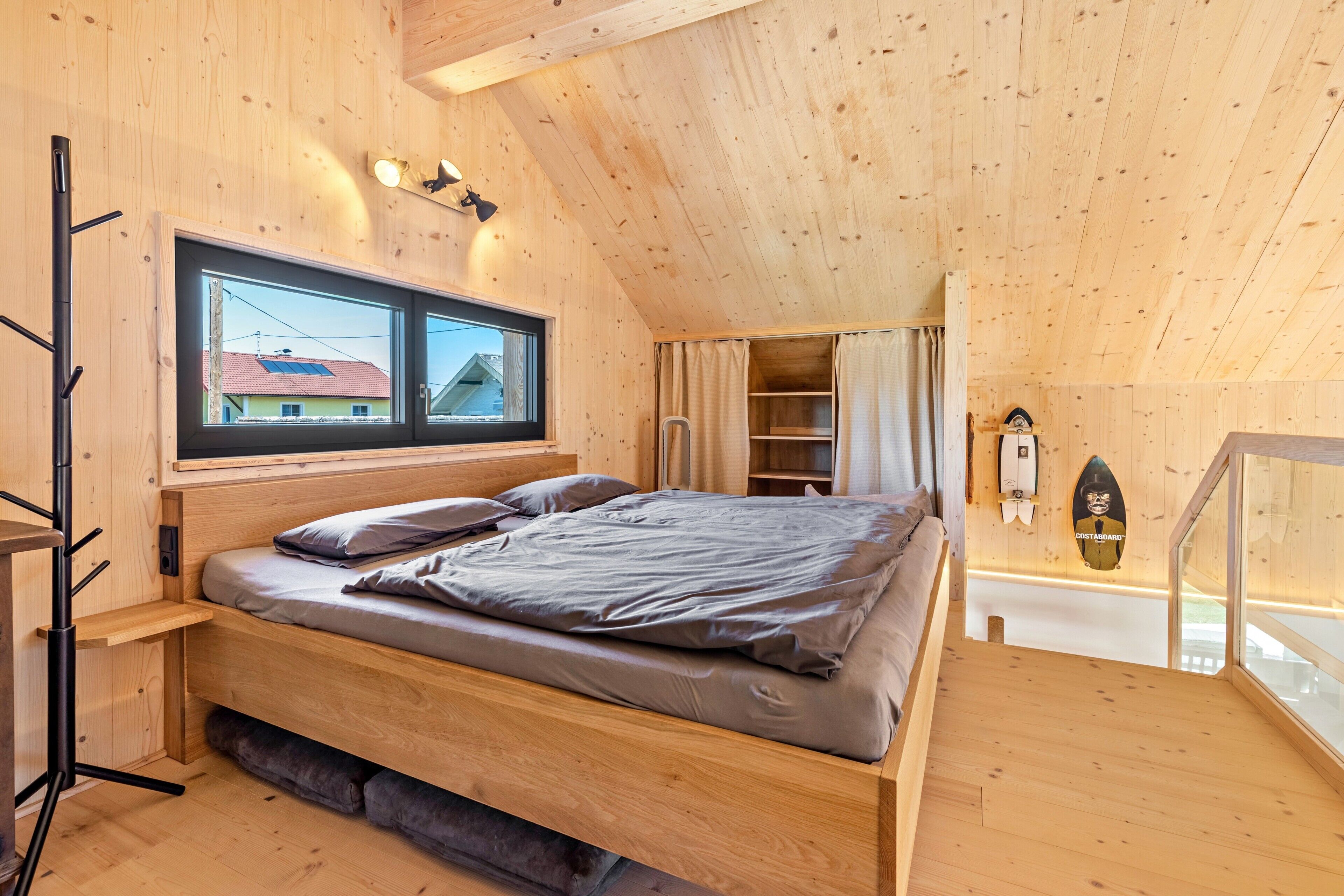 Ein Holzinnenraum mit einem Bett, einem Fenster, einer Leiter und einem Surfbrett als Dekoration.