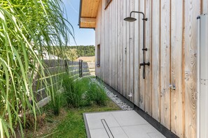Une construction en bois dotée d’une douche, d’un chemin en béton et d’une zone herbeuse avec des plantes.