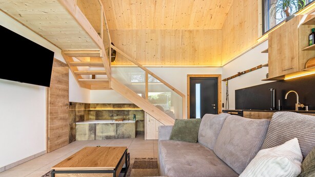 Un interior moderno con una escalera de madera, una cocina y una sala de estar con sofá y mesa de centro.