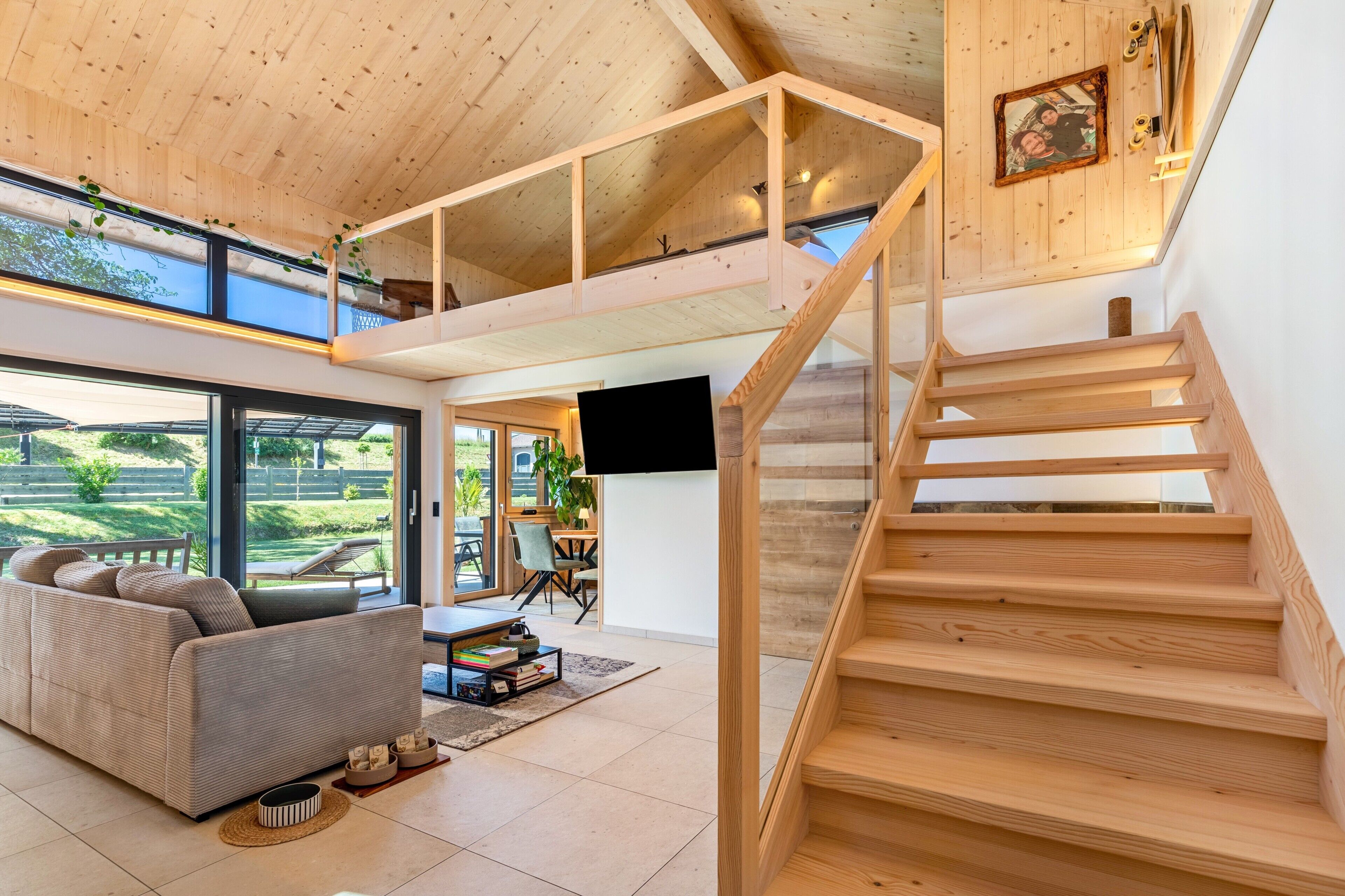 Ein modernes Interieur mit einer Holztreppe, einer Couch und einem Essbereich mit Blick ins Freie.