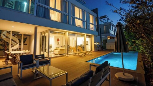Ett modernt hus i två våningar med en swimmingpool, utomhusmöbler och en spiraltrappa.