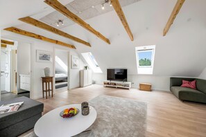 A spacious loft with exposed wooden beams, a flat-screen TV, a green sofa, and a dining area with a white table. - Beautiful holiday home, completely renovated in 2026, located in scenic. (Sønder Felding)