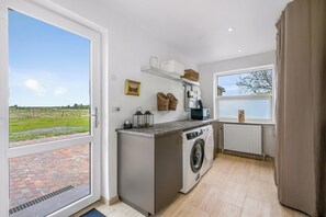 A laundry room with a washing machine, a drying rack, and a window with a view of a green field. - Beautiful holiday home, completely renovated in 2026, located in scenic. (Sønder Felding)