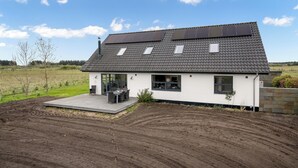 Een modern huis met een schuin dak, zonnepanelen en een terras met tuinmeubilair.