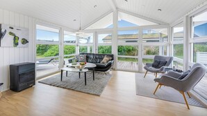A spacious room with a large window, a black leather sofa, two grey armchairs, a small table, and a fireplace. - Lovely holiday home with a wilderness bath, close to the North Sea and. (Ringkøbing)