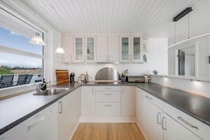 A modern kitchen with white cabinets, a stainless steel range hood, and a large window overlooking a scenic view. - Lovely holiday home with a wilderness bath, close to the North Sea and. (Ringkøbing)