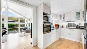 A modern kitchen with white cabinets, a built-in oven, and a large window overlooking a deck. - Lovely holiday home with a wilderness bath, close to the North Sea and. (Ringkøbing)