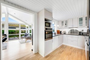 A modern kitchen with white cabinets, a built-in oven, and a large window overlooking a deck. - Lovely holiday home with a wilderness bath, close to the North Sea and. (Ringkøbing)