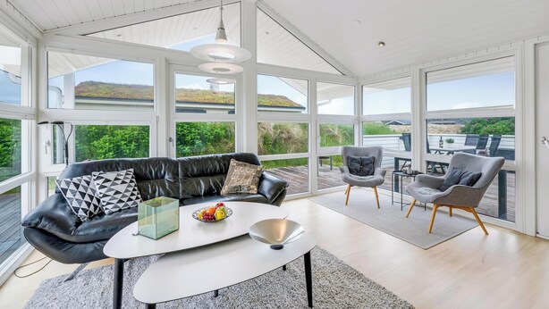 A modern living room with a black leather sofa, a white coffee table, and grey armchairs. - Lovely holiday home with a wilderness bath, close to the North Sea and. (Ringkøbing)