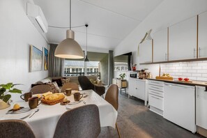 A modern kitchen with white cabinets, a dining area with a table set for two, and a large window providing a view of the city. - Modernized holiday apartment centrally located in Søndervig with 200 meters to. (Ringkøbing)