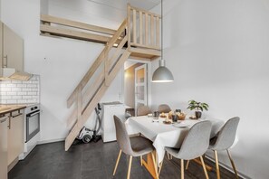Eine moderne Küche mit einer Holztreppe, einem Essbereich mit grauen Stühlen und einer Pendelleuchte.