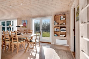 A wooden-paneled room with a dining table, chairs, bookshelves, and a large window. - Bright holiday home with electric charger, terrace and wood-burning stove (Fjerritslev)