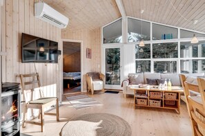 A cozy living room with a fireplace, wooden furniture, a TV, and large windows. - Bright holiday home with electric charger, terrace and wood-burning stove (Fjerritslev)