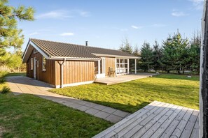 A wooden cabin with a tiled roof, a covered porch, and a grassy yard. - Bright holiday home with electric charger, terrace and wood-burning stove (Fjerritslev)