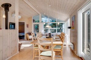 A wooden interior with a dining area, large windows, and a television. - Bright holiday home with electric charger, terrace and wood-burning stove (Fjerritslev)