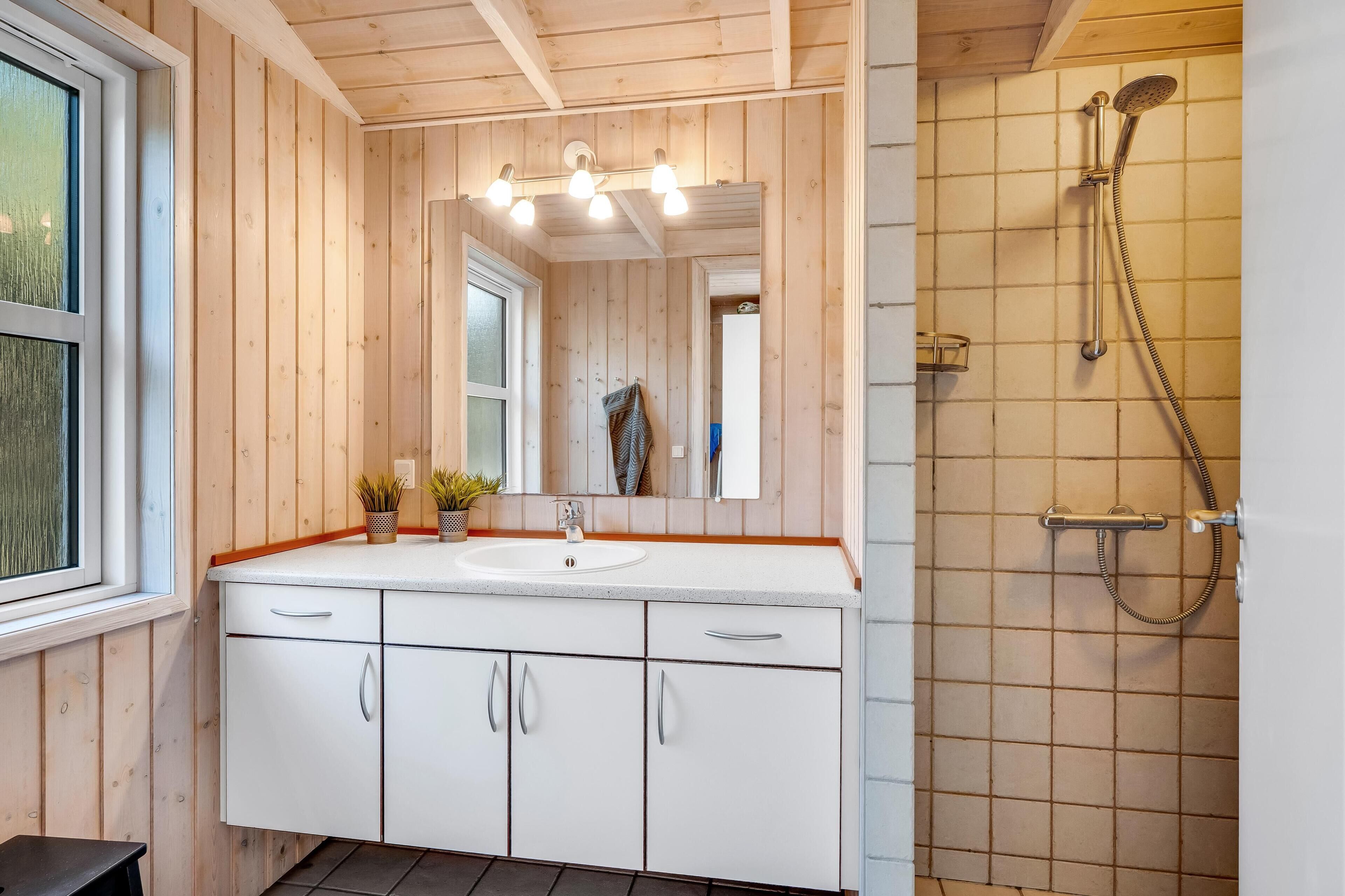 Une salle de bain avec des murs en bois, un lavabo blanc, un miroir et une douche.