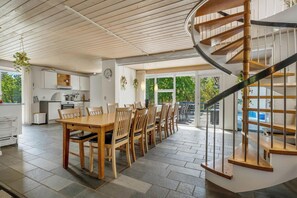 A modern kitchen with white cabinets, a dining area with wooden tables and chairs, and a spiral staircase. - Lovely 16-person pool house with spa, sauna and large terrace (Vestervig)