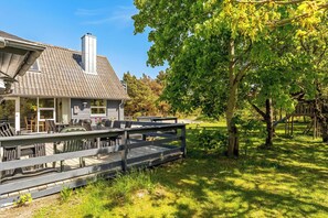 A house with a covered patio, outdoor furniture, and a wooden deck. - Lovely 16-person pool house with spa, sauna and large terrace (Vestervig)